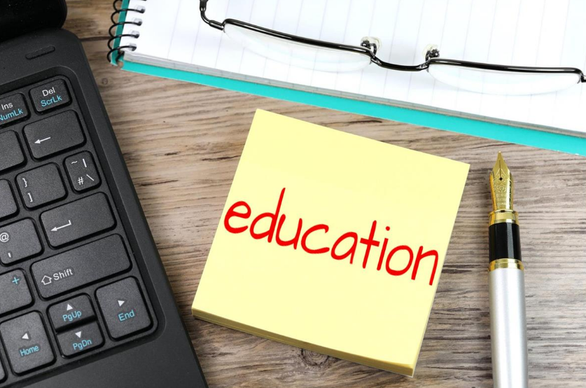 a laptop, a pen, and a notebook with the word “education” on a wooden table